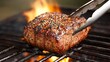 © Slamet - Grilled, seasoned cut of meat over open flame with tongs in BBQ setting