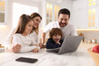 © New Africa - Happy family wearing stylish pajamas looking at laptop at white marble table in kitchen