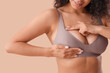 © Pixel-Shot - Young African-American woman checking her breast on beige background, closeup. Cancer awareness concept
