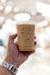© Dontree - Iced latte in a glass in plastic cup on hand. Close up