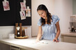 © pixs4u - Asian woman smiling while pouring water from kettle in kitchen