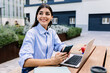 © Xavier Lorenzo - Happy entrepreneur woman with laptop using cell phone sitting outside of office building. Business lifestyle concept.