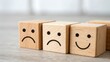 © Annadesign - Wooden cubes with drawn facial expressions showing different emotions sad, neutral, and happy.  Close up view on a light gray surface.  The image