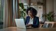 © Favio - 30s Black businesswoman smiling at laptop during video call, home office with minimalist decor and plant background.