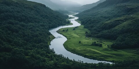 Aufkleber - Aerial view of a meandering river winding through lush green forests and valleys under an overcast sky creates serene landscape scene