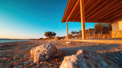 Aufkleber - Beachside cottage under a starry sky with golden light illuminating rocks shore and horizon creating a tranquil scene