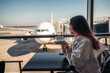 © EdNurg - Passenger drinking coffee looking at airplane through window at airport cafe while waiting for departure