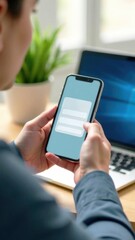 Poster - Person using smartphone to interact with mobile application while sitting at desk with laptop and plant in background, digital communication concept