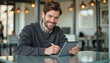 © f_bossa - A portrait headshot photo of a friendly professional CEO executive business worker: A smiling man with a beard sits at a table, using a digital tablet and stylus in a modern cafe setting.