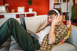 © Miljan Živković - delight young man with headphones lying down on sofa and use laptop