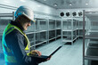© Grispb - Man contractor in cold storage warehouse. Industrial refrigerator with metal racks. Freezer warehouse maintenance engineer. Man with laptop in large freezer. Industrial refrigerator for frozen goods