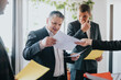 © qunica.com - Group of business professionals examining paperwork and discussing in a collaborative office environment.