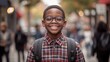 © Wannaeka - Happy African-American boy with backpack walking on city street, wearing glasses and plaid shirt, surrounded by people