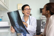 © fizkes - Cheerful senior Caucasian doctor and young African patient woman discussing roentgen image of spine and pelvic bones, talking on consultation meeting, smiling, laughing