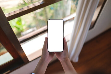 Wall Mural - top view mockup image of a woman holding mobile phone with blank desktop screen at home