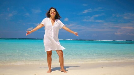 Wall Mural - a woman in a white dress stands on a beach with calm waves and clear sky