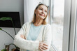 © shurkin_son - Tender romantic senior woman in cardigan and glasses on her head leaning shoulder against window, standing with crossed hands, admiring landscape outside, self-reflecting or recollecting memories
