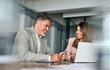 © insta_photos - Happy professional mature businessman and businesswoman executive colleagues of middle age in suits sitting at table having partnership business discussion using laptop at corporate meeting in office.