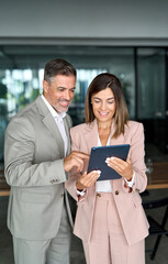 Fototapete - Corporate managers talking meeting working together in lobby. Two mature professional executives colleagues business people looking at tablet computer having conversation standing in office, vertical.