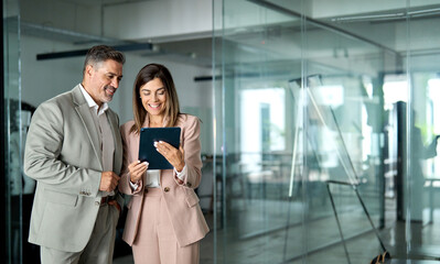 Fototapete - Professional business executives team working using digital tablet computer standing in office. Two middle aged colleagues managers discussing smart technology at corporate meeting. Copy space.