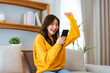 © Monster Ztudio - Happy young asian woman relax on comfortable couch at home texting messaging on smartphone, smiling girl use cellphone, chatting online message, shopping online from home