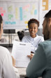 © fizkes - Happy African American job applicant woman meeting with two employers for interview talk, sitting at table in blurred background, HR managers reviewing paper resume. Vertical shot