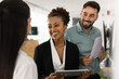 © fizkes - Happy diverse business partners talking at whiteboard, discussing collaboration, partnership terms, smiling, laughing, holding tablet, paper financial report, meeting for negotiation
