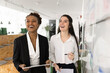 © fizkes - Two cheerful female office colleagues working together at Kanban board, looking away and laughing, talking to coworkers away, having fun, discussing creative ideas for project, enjoying teamwork