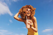 © SHOTPRIME STUDIO - Happy young woman with curly hair enjoying a smoothie at the beach under a blue sky