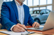 © zinkevych - Businessman sitting in dealership office singing automobile contract processing car sale