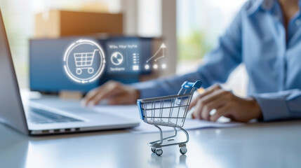 Poster - miniature shopping cart sits on desk beside laptop, symbolizing online shopping and e commerce. person is working in background, highlighting digital transactions