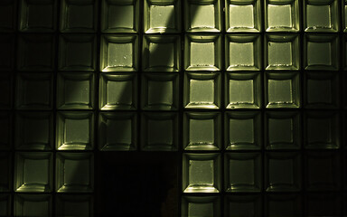 Aufkleber - A wall of green rectangular tiles with a textured surface is partially lit, casting dramatic shadows and highlights. The light emphasizes the geometric pattern.
