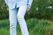 © HalynaRom - A person stands in lush green grass, showing grass stains on their white jeans. The bright sunlight highlights the vibrant colors of the outdoor setting, suggesting playful activities.
