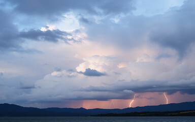Poster - Dramatic storm clouds fill the sky with flashes of lightning illuminating distant mountains above a body of water.