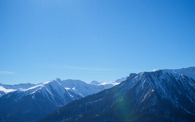Poster - A majestic mountain range stands tall under a vast clear blue sky. Snow covers the peaks, contrasting with the dark slopes below in a serene landscape.