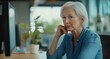 © Gnublin - Confident mature woman in her fifties sitting at an office desk, looking thoughtful. Professional work environment with computer and plant in background.