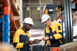 © Wanwajee - African American and White employee looking and pointing at tablet , worker in yellow collar talking beside folk lift and cardboard box in warehouse.  Two men work in logistic industry.