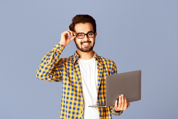 Poster - Happy Indian guy in glasses using laptop computer for distance work or education on lilac background, panorama