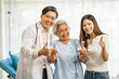 © Wanwajee - Senior elderly woman delighted after receiving treatment at clinic. Physician doctor and young lady standing beside old patient smile and laugh and showing thumb up, looking at camera.