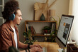 © TrueFrame Collective - Side view of joyful young biracial man in headphones generating images using artificial intelligence on desktop computer