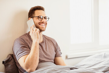 Aufkleber - Guy Talking On Cellphone Calling Having Phone Conversation Sitting In Bed At Home. Man Speaking On Smartphone In Bedroom. Mobile Communication Concept. Free Space