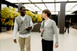 © Drobot Dean - A young black man and a white man walk side by side in the modern office lobby, casually talking and holding laptops and a bag. Business context with professional attire and bright space.