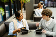 © Drobot Dean - A White young man and an Indian young woman with glasses enjoying lunch together during their internship in a modern office space, engaging in conversation while working in a friendly environment.
