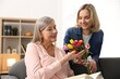 © New Africa - Smiling daughter congratulating her mom with bouquet of tulips at home. Happy Mother's Day