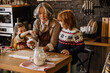 © Drobot Dean - An elderly White woman baking with two school-aged children in a kitchen, using measuring cups and cookie cutters on a floured wooden surface near holiday decorations.