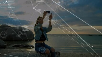 Poster - Woman sitting on rock by sea with digital network animation overlay