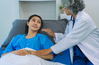 © ArLawKa - An elderly Asian female doctor is writing on a clipboard with a young female patient in a hospital room.