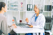 © ArLawKa - An elderly Asian female doctor is writing on a clipboard with a young female patient in a hospital room.