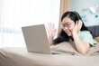 © Surachetsh - Beautiful Asian woman using zoom meeting and making facetime video, social distancing during covid pandemic period on her bedroom with a pastel green - brown color theme.