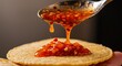 © JustFun - Close-Up of a Hand Spoonful of Delicious Red Chili Sauce Dripping Onto a Round Crispy Snack, Showcasing the Texture and Vibrancy of the Sauce.